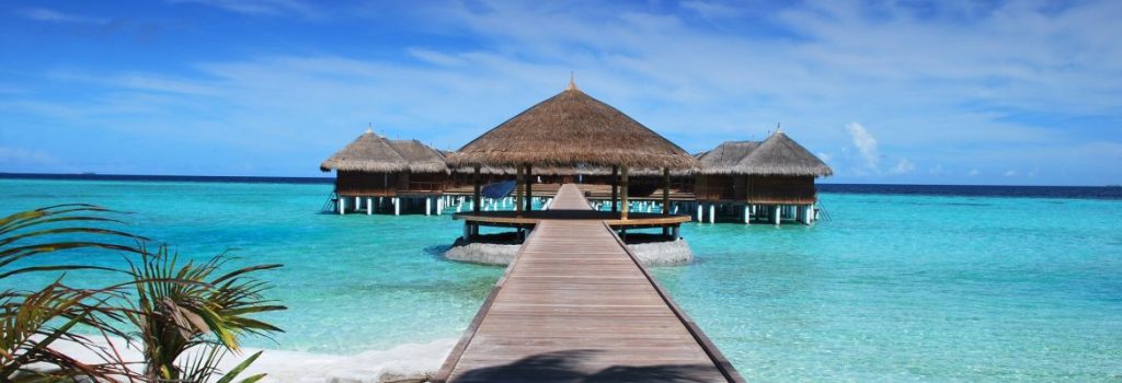 Brown beach hut in the ocean with a walkway over the water