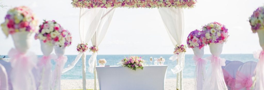 Wedding gazebo decorated with flowers and voile on a sunny beach with a view of the ocean.