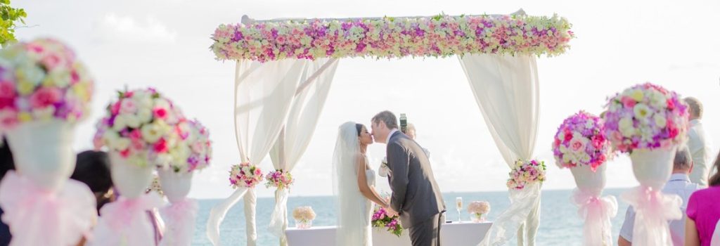 Couple getting married on a tropical beach under a flower gazebo