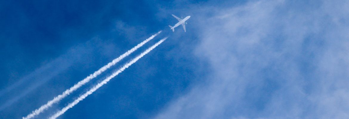 Airplane in a blue sky showing the contrails behind.